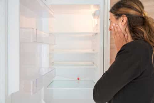 une femme effrayée par son réfrigérateur vide, image symbolisant la peur de ne pas pouvoir acheter un bien immobilier sans apport