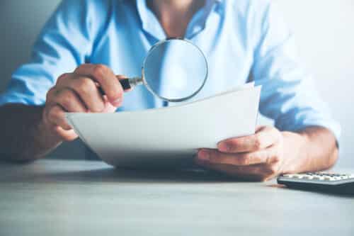 une homme regarde avec une loupe un dossier de demande de crédit immobilier