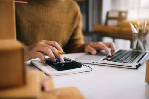 gros plan sur un bureau, une femme fait des calculs avec un ordinateur et une calculatrice, elle estime son capital mobilier