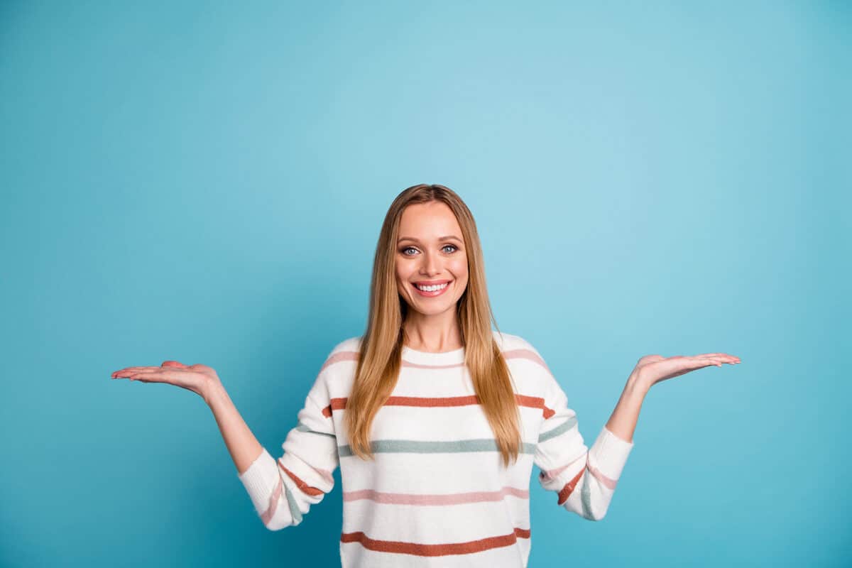 une femme souriant sur fond bleu avec ses mains elle imite une balance de pesée comme si elle estimait le pour et le contre d'un projet ou d'un contrat d'assurance emprunteur