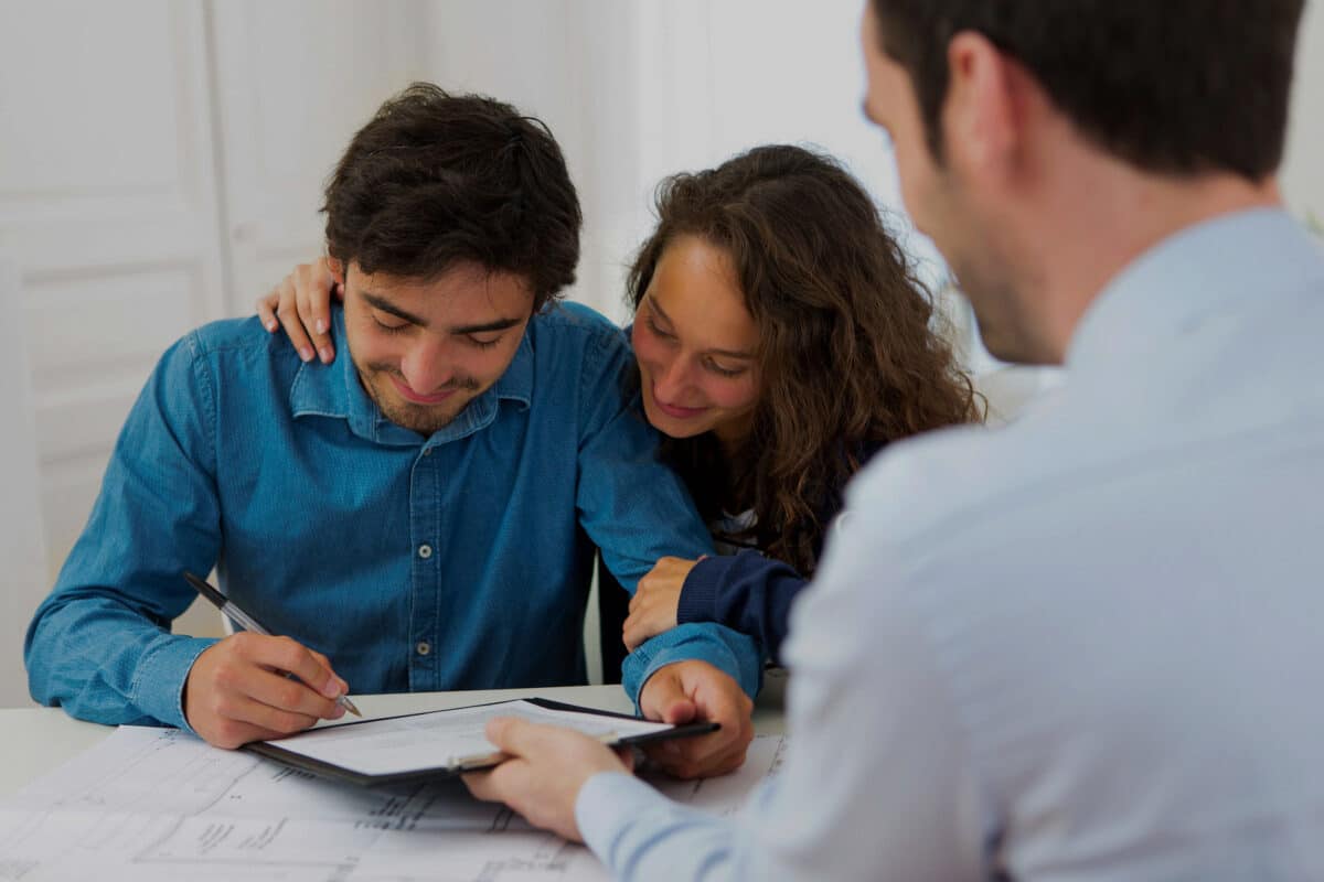 un couple souriant signe une proposition de prêt devant un professionnel du crédit