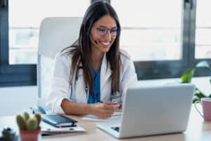 une jeune femme médecin installée à son bureau sourit en regardant son ordinateur, elle découvre les possibilités du rachat de crédit pour fonctionnaire