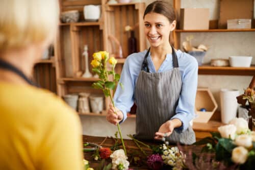 une fleuriste souriante présente un bouquet de rose à une cliente, elle semble heureuse de povoir regrouper ses crédits