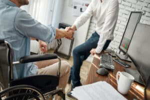en gros plan poignée de main entre un homme en fauteuil roulant et une femme valide, un symbole de solidarité