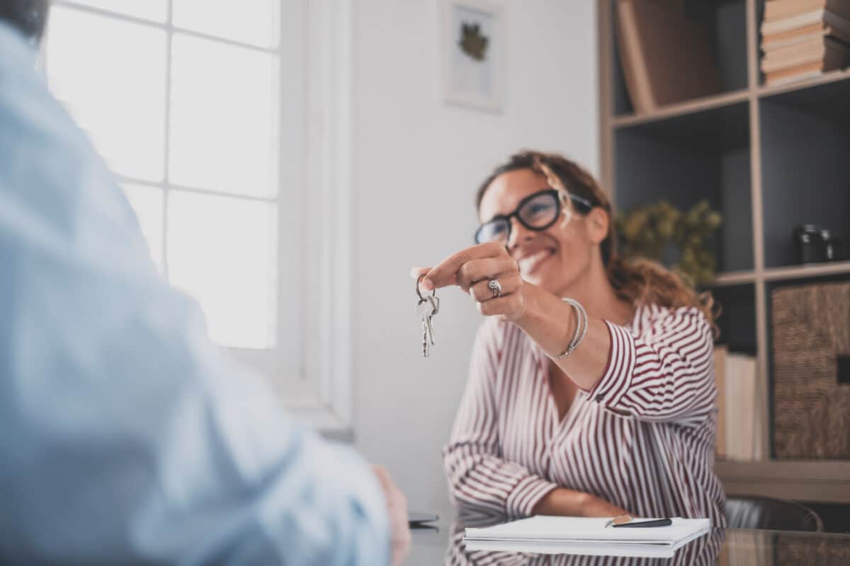 une femme agent immobilier souriante tend les clefs d'un appartement à un futur locataire