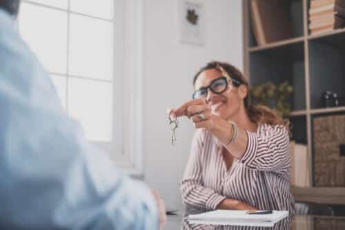 une femme agent immobilier souriante tend les clefs d'un appartement à un futur locataire