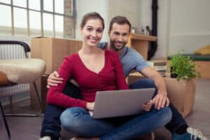 un jeune couple souriant dans son salon, ils ont la possibilité de faire un rachat de crédit pour locataire