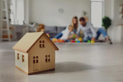 un couple joue avec ses enfants dans son appartement en avant plan une maquette de maison
