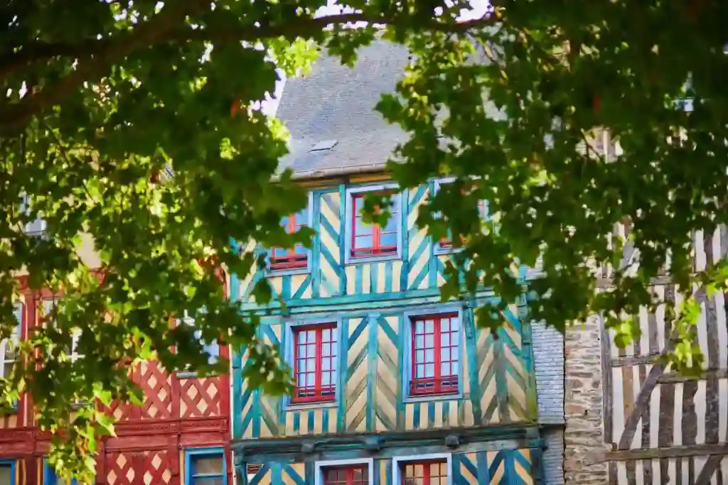 À Rennes, maisons à colombages très colorées à travers des arbres au feuillage vert.