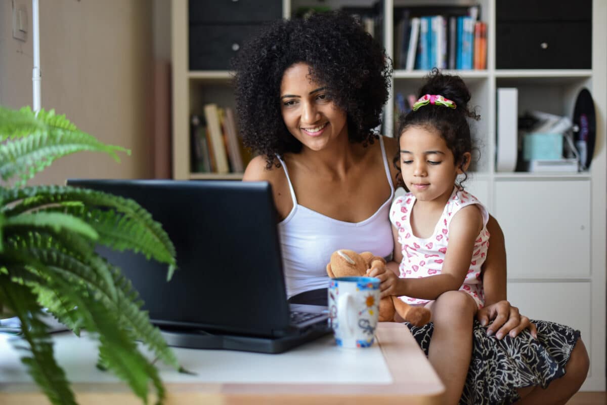 une femme avec sa fille dans les bras consulte un ordinateur assise, elle vient d'apprendre une bonne nouvelle