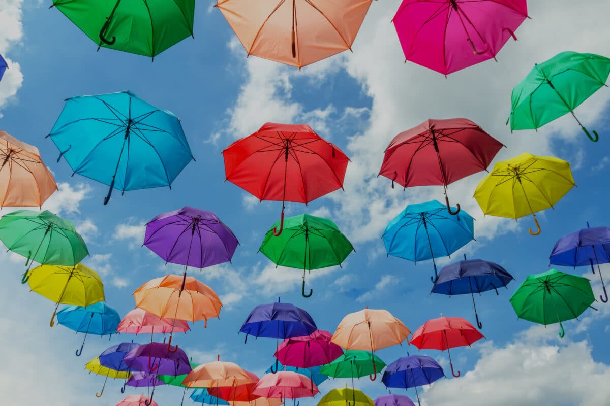 Installation d'artiste : des parapluies multicolores sont en lévitation sur arrière plan de ciel ensoleillé