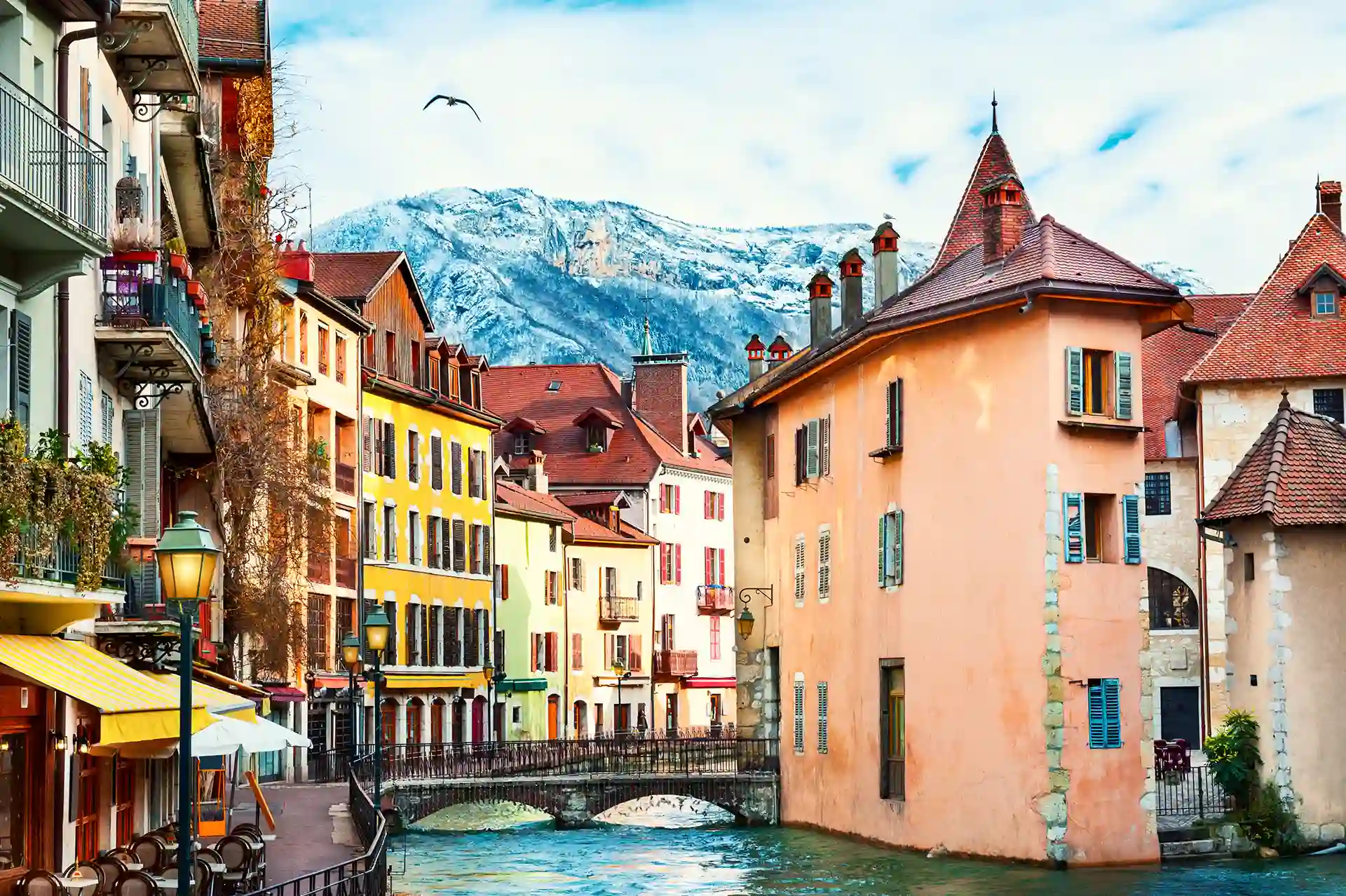 Investir à Annecy en 2025. La photo montre des logements colorés situés dans la vieille ville et les Alpes en toile de fond.
