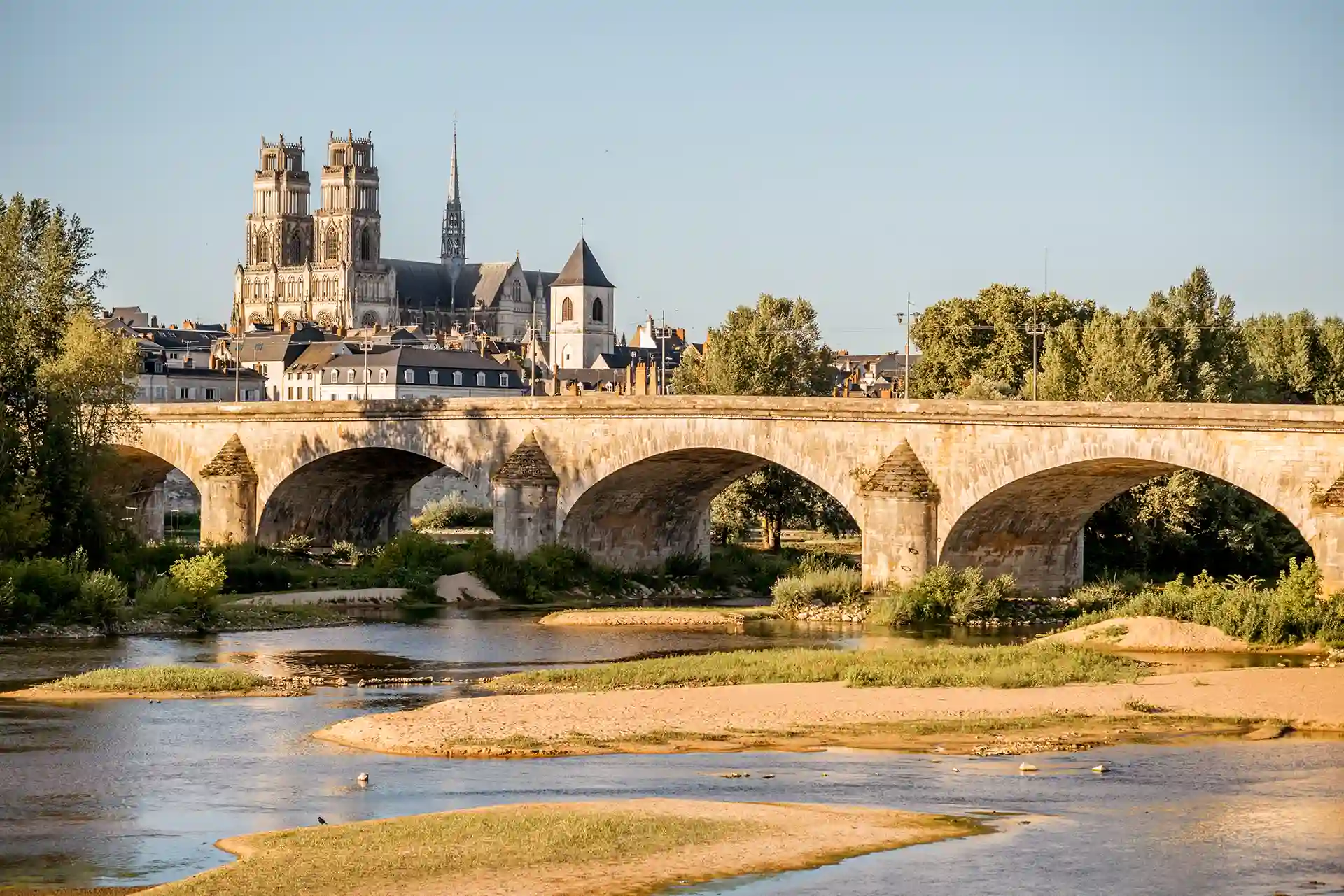 Acheter ou vendre un bien immobilier à Orléans pour y habiter ou le louer en 2025. L'image montre un pont chevauchant la Loire avec une vue sur la cathédrale Sainte-Croix.